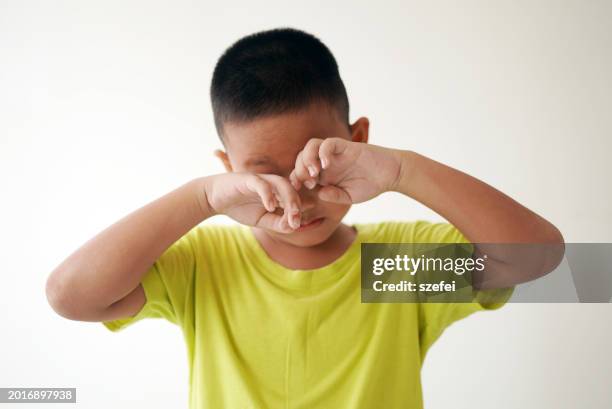 child rubbing eyes standing on plain background - tired eyes stock pictures, royalty-free photos & images