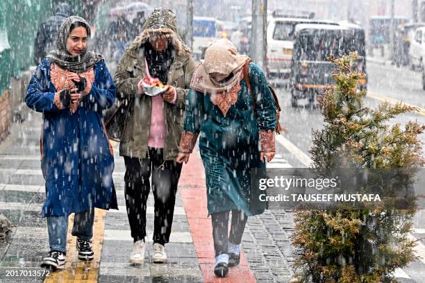 Women walk along a pavement amid snowfall in Srinagar on February 20, 2024.