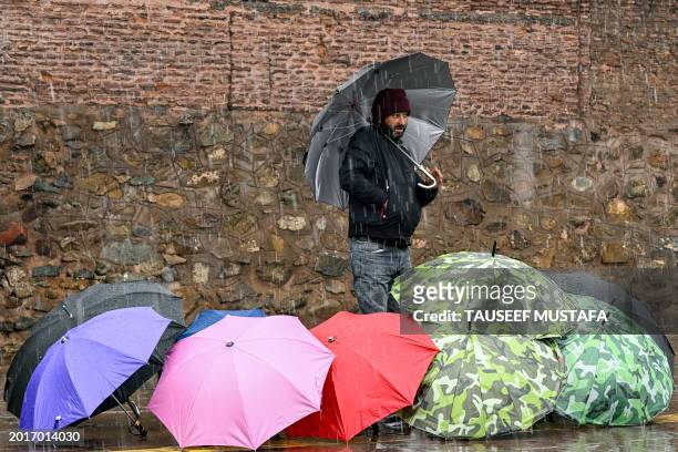 An umbrella vendor waits for customers along a roadside amid rainfall in Srinagar on February 20, 2024.