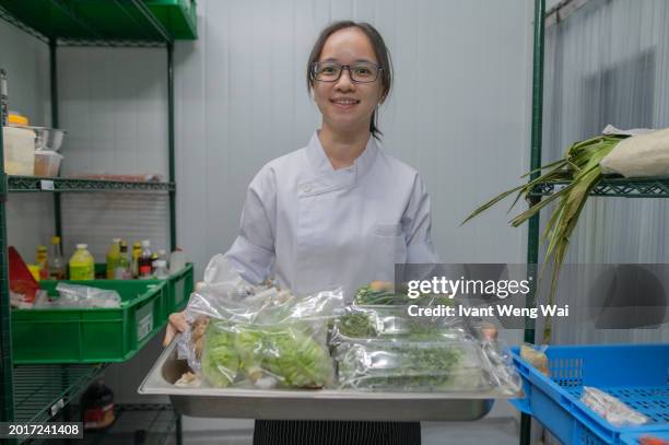 asian female apprentice kitchen holding vegetable pan - restaurant kitchen fridge stock pictures, royalty-free photos & images