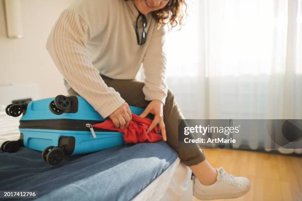 woman packing full suitcase in a hotel room. summer travel and tourism concept. - stuffed stock pictures, royalty-free photos & images