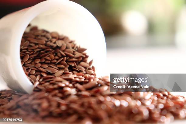 close-up of raw flax seeds pouring out from a white ceramic bowl/white background/still life - semilla-de-lino fotografías e imágenes de stock