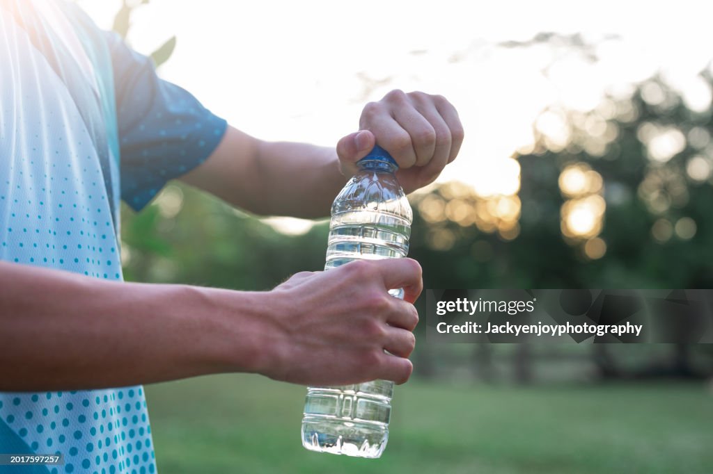 Young man drinking water and taking a break after running in park
