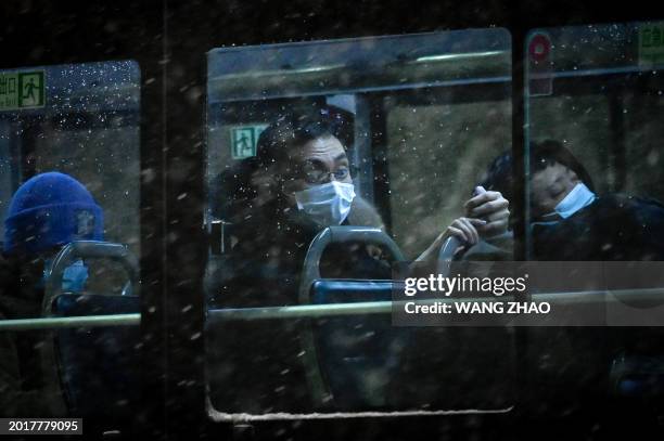 Man looks out through the window of a bus on a snowy night in Beijing on February 20, 2024.
