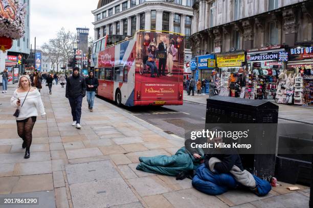 Two men under sleeping bags living on the street beside a King Charles III Coronation bus advert for tourist attraction Madame Tussauds at Piccadilly...