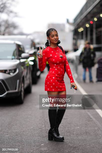 Guest wears long bejeweled earrings, a silver heart-shaped necklace, a mini dress with polka dots, thigh high leather boots , outside Area, during...