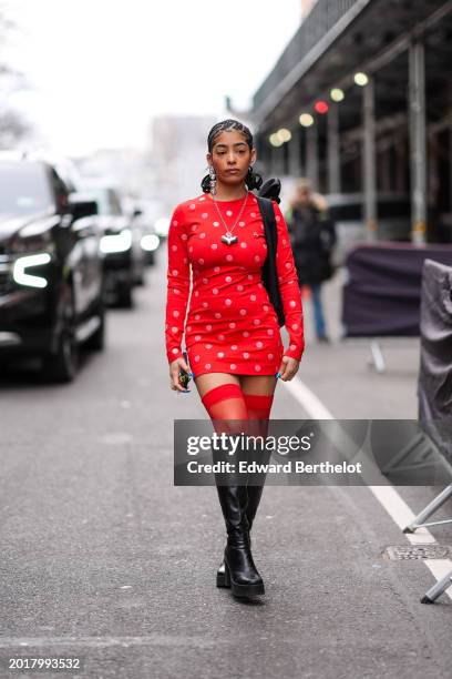 Guest wears long bejeweled earrings, a silver heart-shaped necklace, a mini dress with polka dots, thigh high leather boots , outside Area, during...