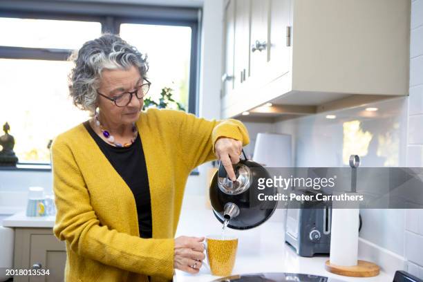 mature woman making a hot drink in a domestic kitchen - making coffee stock pictures, royalty-free photos & images