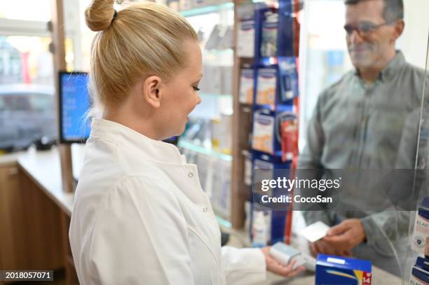 female pharmacist serving the customer, customer is paying contactless with credit card - coco stock pictures, royalty-free photos & images