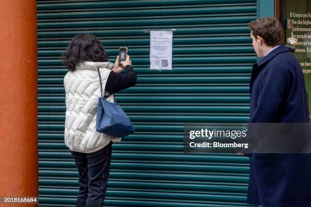 Passerby takes a photograph of the closure notice on the shutters of an outlet of The Body Shop on Bond Street in central London, UK, on Tuesday,...