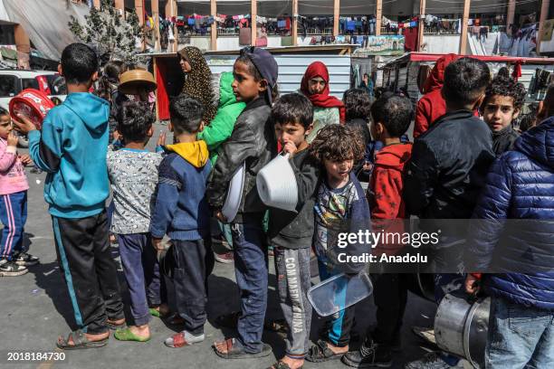 Palestinian children, holding empty pots, wait in line to receive hot meal prepared by volunteers for Palestinian families ,displaced to Southern...