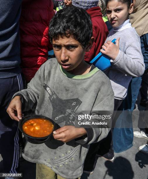 Palestinian child carries food with a bucket after receiving hot meal prepared by volunteers for Palestinian families ,displaced to Southern Gaza due...