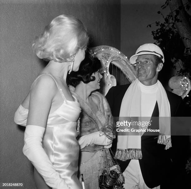 American actress Carroll Baker, wearing an evening gown with evening gloves, in conversation with American actor Charlton Heston at a 'Jean Harlow'...