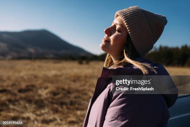 frau genießt sonnigen tag in der natur mit bergen im hintergrund - einatmen stock-fotos und bilder