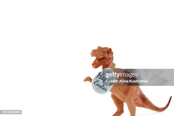 toy dinosaur holding wooden egg with lettering - happy easter on white background - dinosaur background stock pictures, royalty-free photos & images