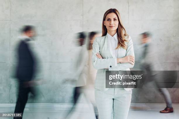 junge geschäftsfrau steht im büro, während menschen in verschwommenen bewegungen herumlaufen - bewegungsunschärfe büro stock-fotos und bilder