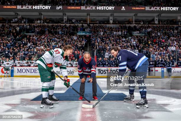 Winnipeg Jets alumni Bill Riley drops the puck between Adam Lowry and Kirill Kaprizov of the Minnesota Wild during the ceremonial face-off on Black...