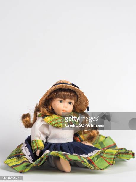 In this photo illustration, a vintage Austrian porcelain doll little girl with blue eyes, and curly brown hair, wearing a white skirt with a...