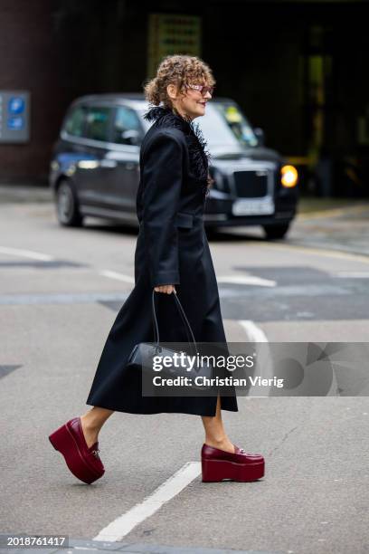 Guest wears black Alaia bag, red platform shoes, black coat outside 16Arlington during London Fashion Week February 2024 on February 17, 2024 in...