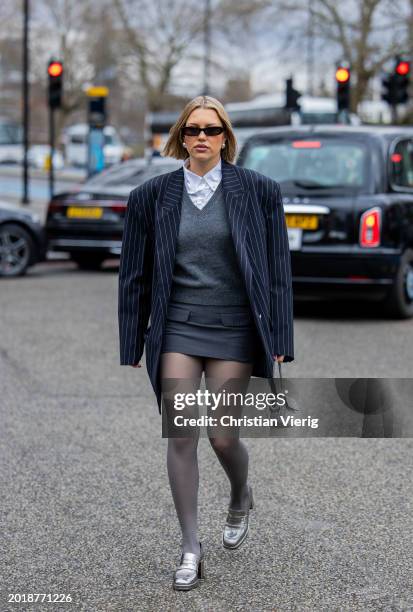 Caroline Ebo wears navy striped oversized blazer, grey v neck jumper, skirt, tights, bag with rhinestones, silver shoes, white button shirt outside...