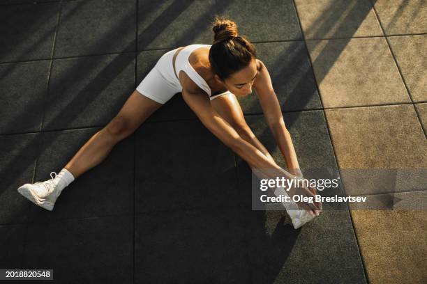 top view of sportive woman stretching legs on sports ground. street workout concept - strekken stockfoto's en -beelden