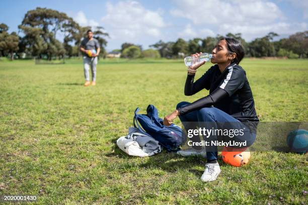 jugadora de fútbol adolescente tomando un descanso y bebiendo agua en un campo de deportes - niño-tomando-agua fotografías e imágenes de stock
