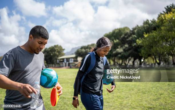 young male coach with teenage girl soccer player leaving the field after practice session - south africa training session stock pictures, royalty-free photos & images