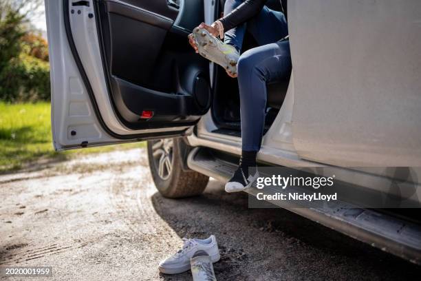 young girl soccer player removing soccer shoes sitting a car after practice session - south africa training session stock pictures, royalty-free photos & images