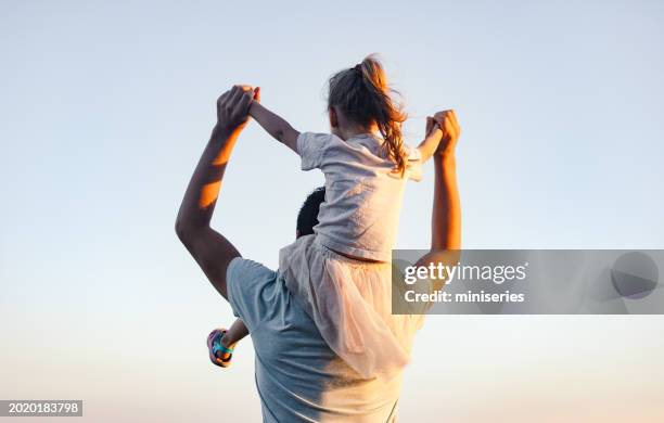 back view of a father carrying his daughter on his shoulders - child on mans shoulder stock pictures, royalty-free photos & images