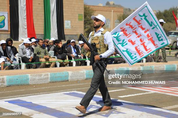 Student among many recruited into the ranks of Yemen's Huthi group holds an automatic rifle as he walks over a giant Israeli flag during a rally in...