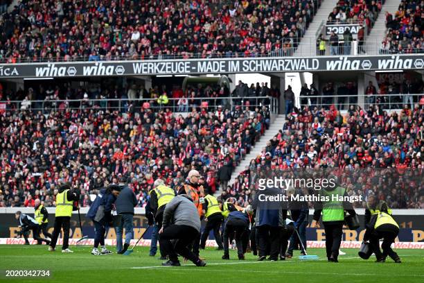 Stewards pick up chocolate coins from the pitch after a protest during the Bundesliga match between Sport-Club Freiburg and Eintracht Frankfurt at...