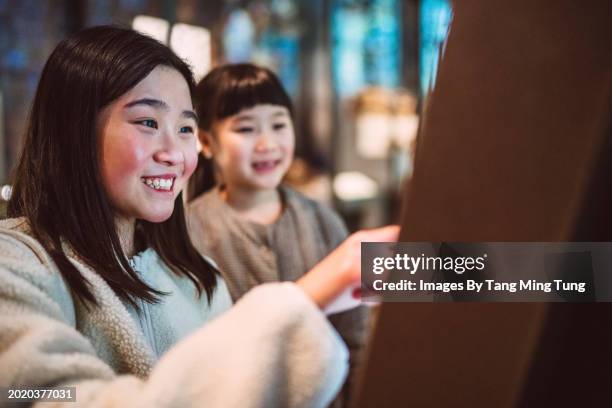 cheerful teenage girl using the interactive touch screen while checking out exhibits with her younger sister in a public museum - musée historique photos et images de collection