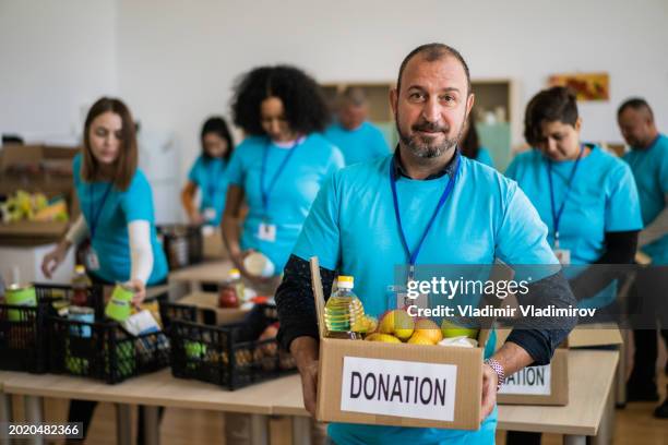 a male charity worker holding a box of donated food - man holding donation box stock pictures, royalty-free photos & images