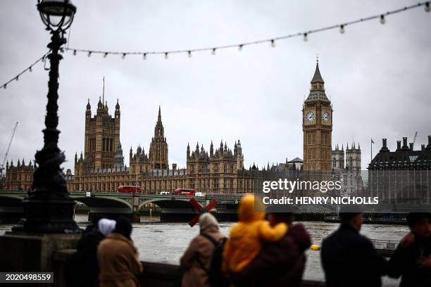 Pedestrians walk under the rain along the Southbank by the River Thames, with The Elizabeth Tower, commonly known by the name of the clock's bell...