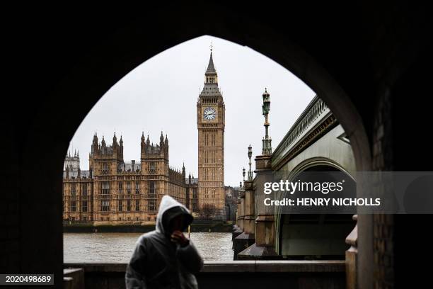 Pedestrian walks under the rain along the Southbank by the River Thames, with The Elizabeth Tower, commonly known by the name of the clock's bell...