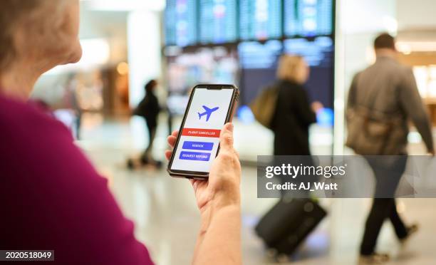 mature woman getting a flight cancellation notification on her phone at the airport - cancellation stock pictures, royalty-free photos & images