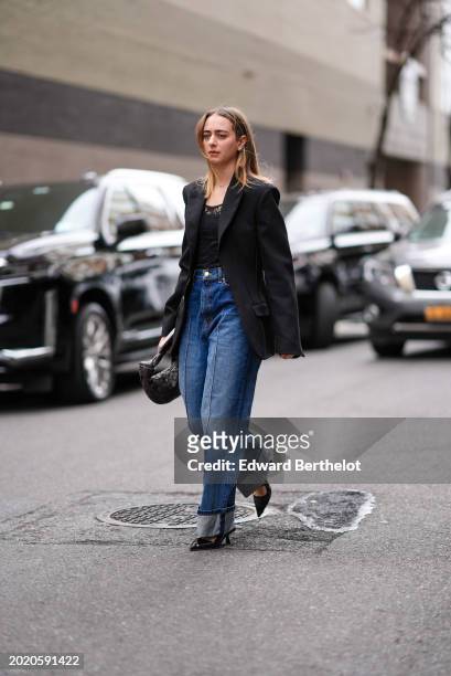 Guest wears a black oversized blazer jacket, a black top with floral embroidery, long wide-leg blue denim jeans pants , a black woven leather bag,...