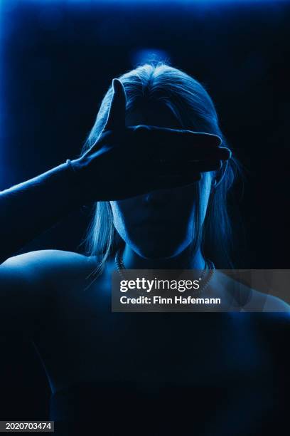 depressed woman with her right hand over her eyes. blue neon lights on her body from her front shirtless shown only the part over her breast - rim light portrait stock pictures, royalty-free photos & images