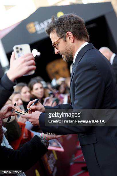 Bradley Cooper signs an autograph for a fan during the EE BAFTA Film Awards 2024 at The Royal Festival Hall on February 18, 2024 in London, England.