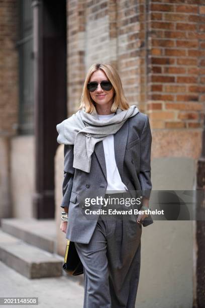 Lisa Aiken wears a light gray scarf, a dark gray oversized blazer jacket, a white t-shirt, matching suit pants, a black leather bag, outside Proenza...