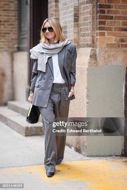 Lisa Aiken wears a light gray scarf, a dark gray oversized blazer jacket, a white t-shirt, matching suit pants, a black leather bag, outside Proenza...