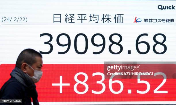 Man walks past an electronic board displaying the Nikkei index of the Tokyo Stock Exchange above 39000 points on a street in Tokyo on February 22,...