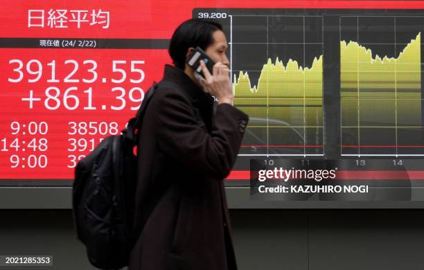 Man walks past an electronic board displaying the Nikkei index of the Tokyo Stock Exchange above 39000 points on a street in Tokyo on February 22,...