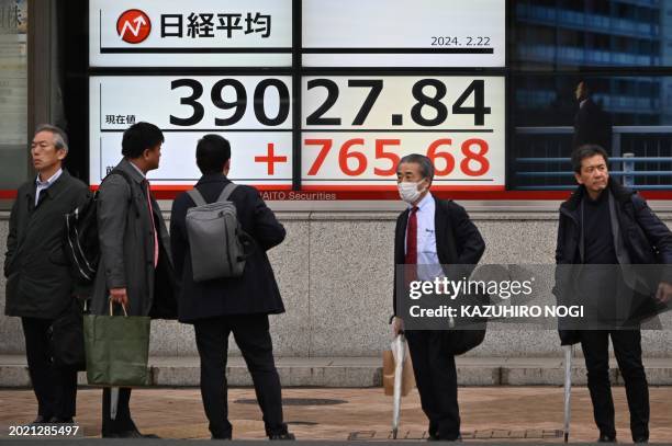 Pedestrians look at an electronic board displaying the Nikkei index of the Tokyo Stock Exchange above 39000 points on a street in Tokyo on February...