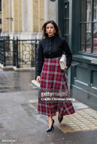 Bettina Looney wears black cardigan, white bag, high waisted red checkered skirt outside Emilia Wickstead during London Fashion Week February 2024 on...