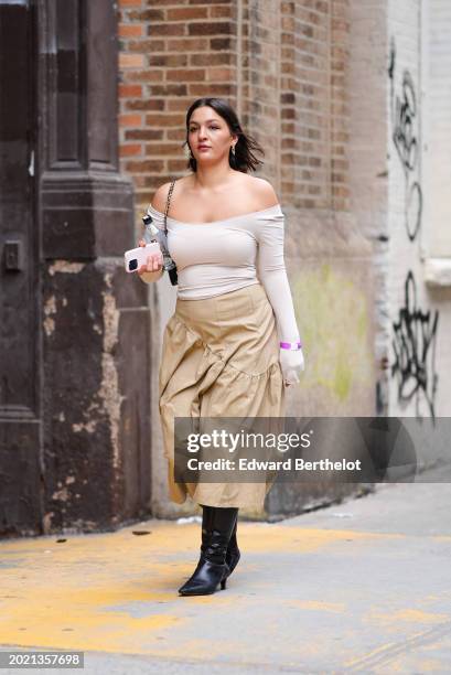 Guest wears earrings, a white off-shoulder gathered top with integrated gloves, a beige gathered midi skirt, kitten heels black leather pointed boots...