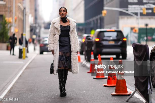 Guest wears a hair bun, dark lipstick , make-up, a floral detail choker, a white long fluffy faux fur coat , a low neck black dress with mesh...