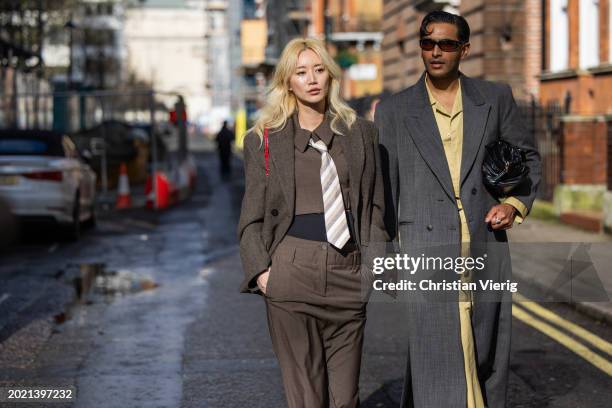 Betty Bachz wears brown jacket, tie, pants, shirt & Rahi Chadda wears grey coat, black bag, beige overall outside Eudon Choi during London Fashion...