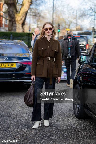Model wears brown belted jacket, black white striped pants, brown bag outside Holzweiler during London Fashion Week February 2024 on February 18,...