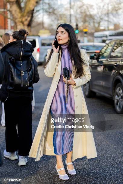 Guest wears beige coat, pink striped dress, black Chanel bag outside Holzweiler during London Fashion Week February 2024 on February 18, 2024 in...